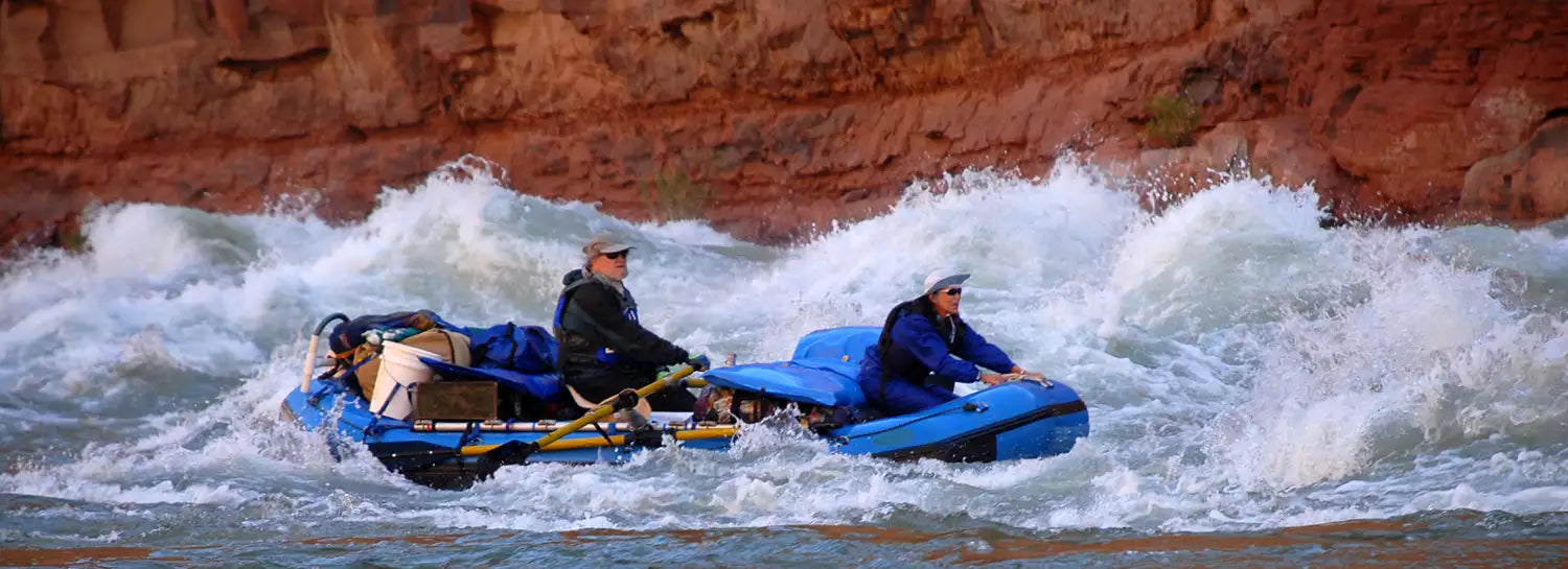 Two people rafting down rapids in a blue raft.